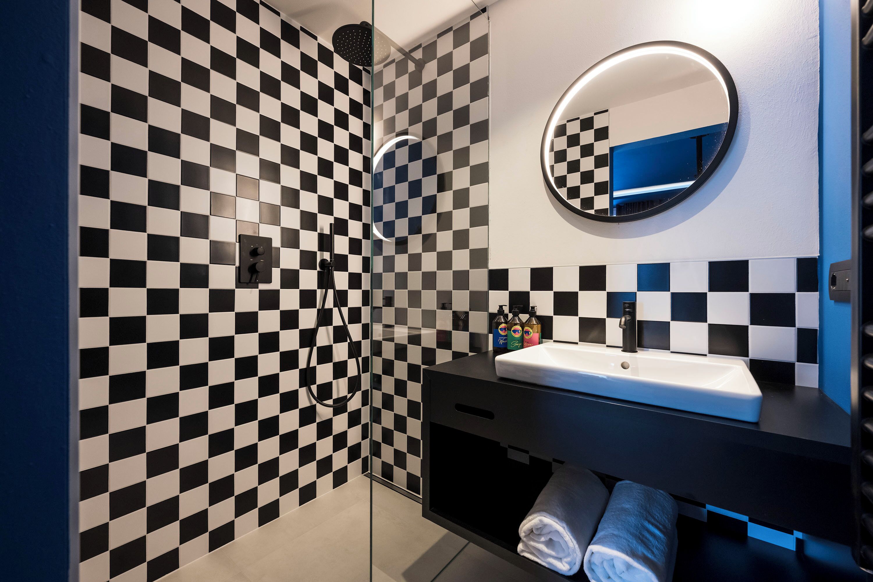 A modern bathroom with a checkered tile wall, a round mirror, a sink, and a towel rack.