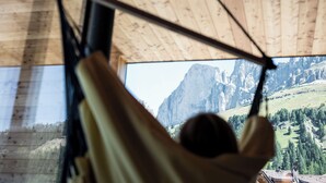 A hammock suspended from a ceiling with a view of a mountainous landscape through a window.
