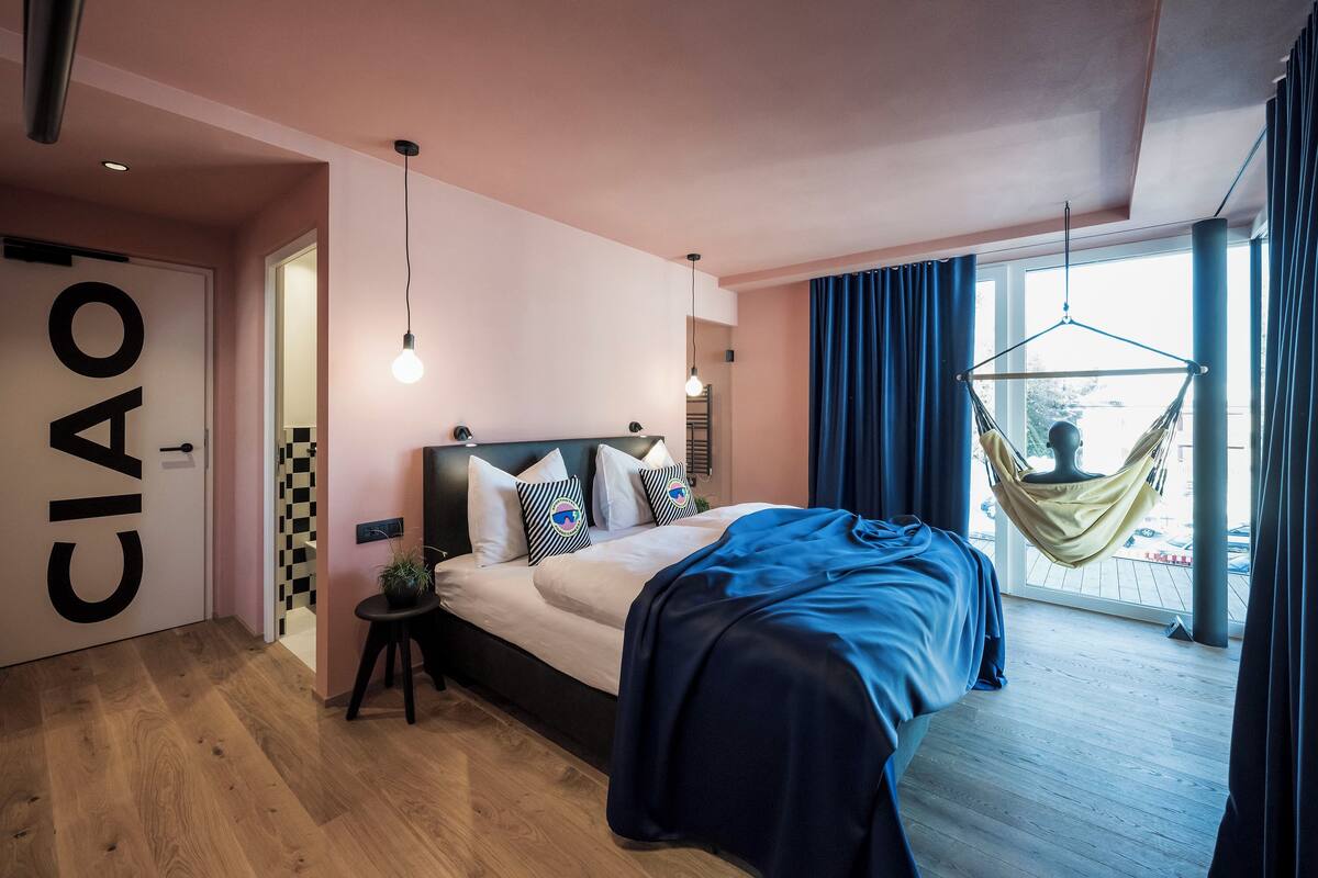 Une chambre moderne avec un lit, un fauteuil suspendu et une vue sur l’extérieur.