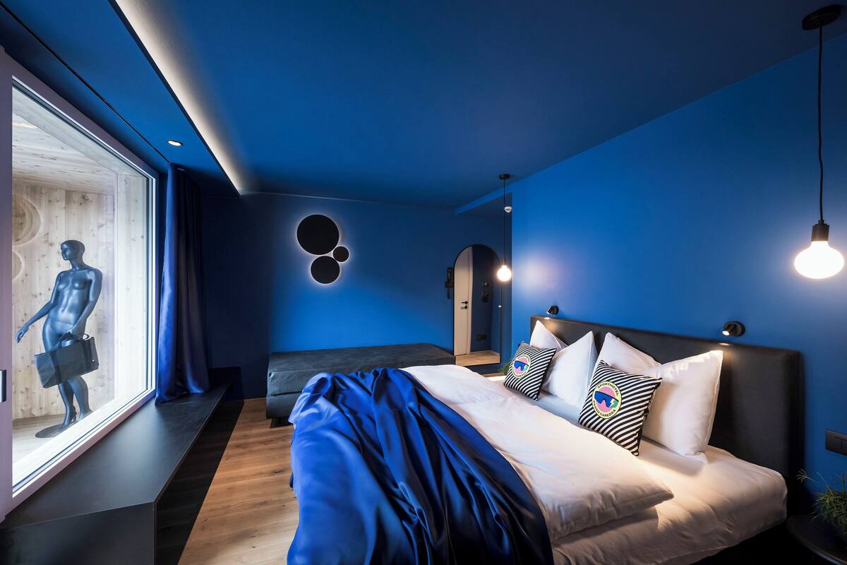 Une chambre moderne avec un grand lit, une fenêtre ornée d’un mannequin et un décor mural original.