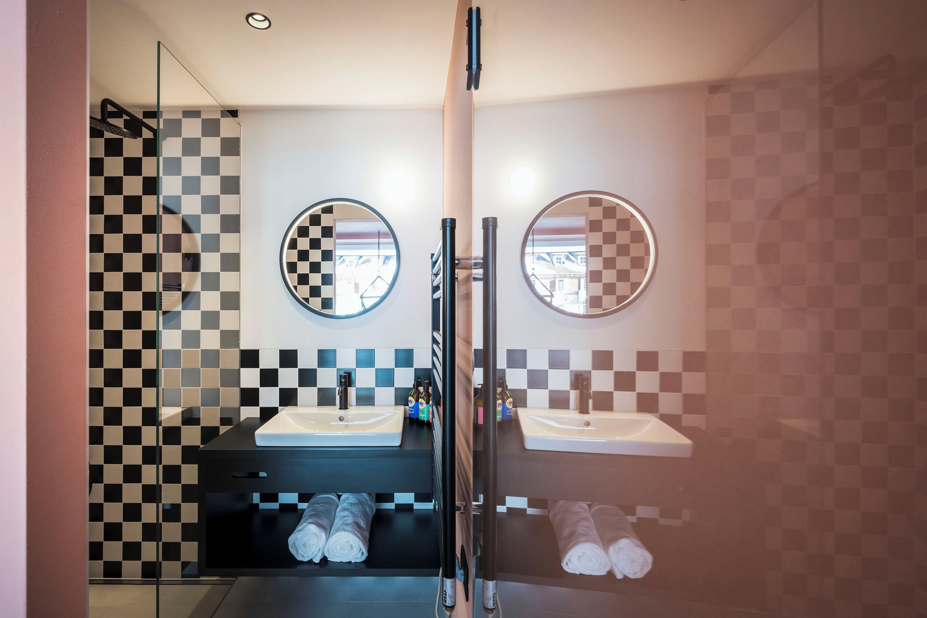 A modern bathroom with checkered tile walls, two sinks, and a glass shower enclosure.