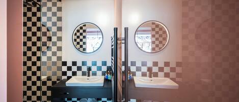 A modern bathroom with checkered tile walls, two sinks, and a glass shower enclosure.