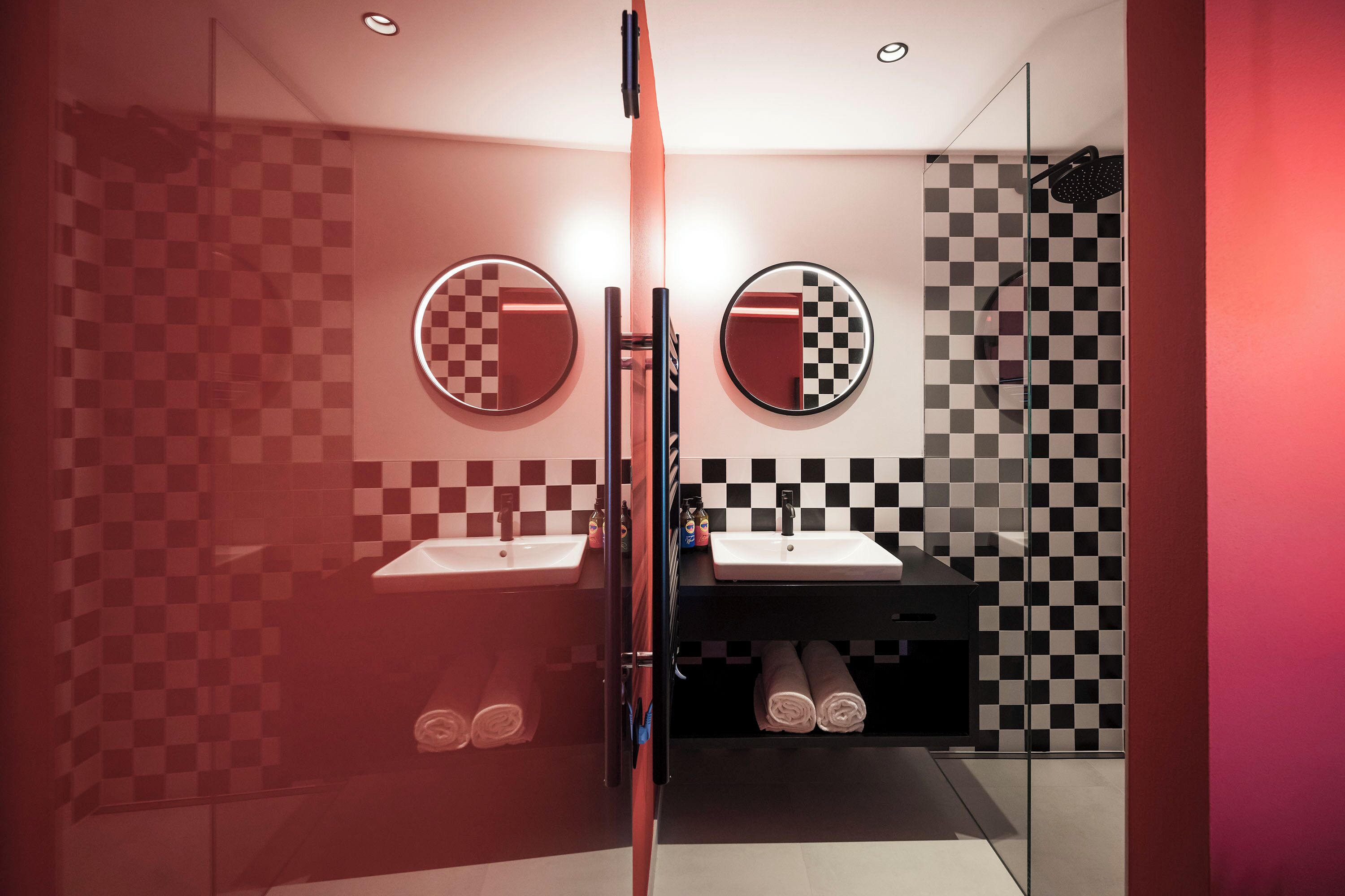 A modern bathroom with checkered walls, two sinks, and a glass shower enclosure.