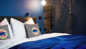 A bed with striped pillows, a headboard, a wall-mounted light, and a checkered wall pattern.