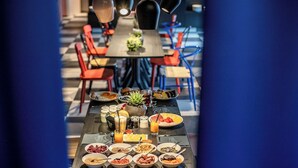 Una tavola da pranzo con diversi cibi e bevande per la colazione, circondata da sedie e lampade a sospensione.