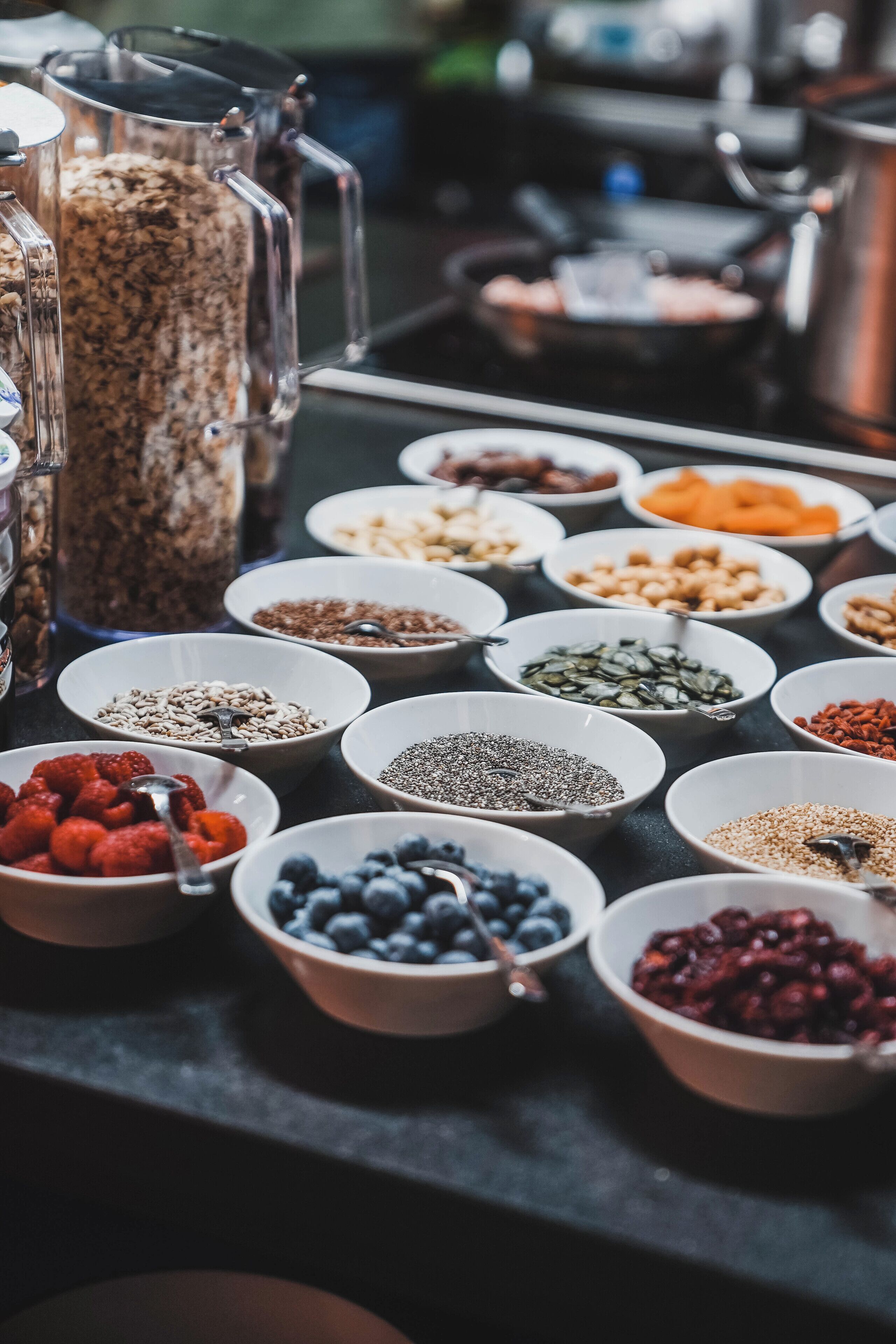 A variety of bowls containing different types of nuts, seeds, and dried fruits on a table.