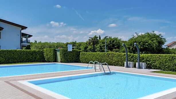 A swimming pool with two lanes, surrounded by a hedge and a paved walkway.