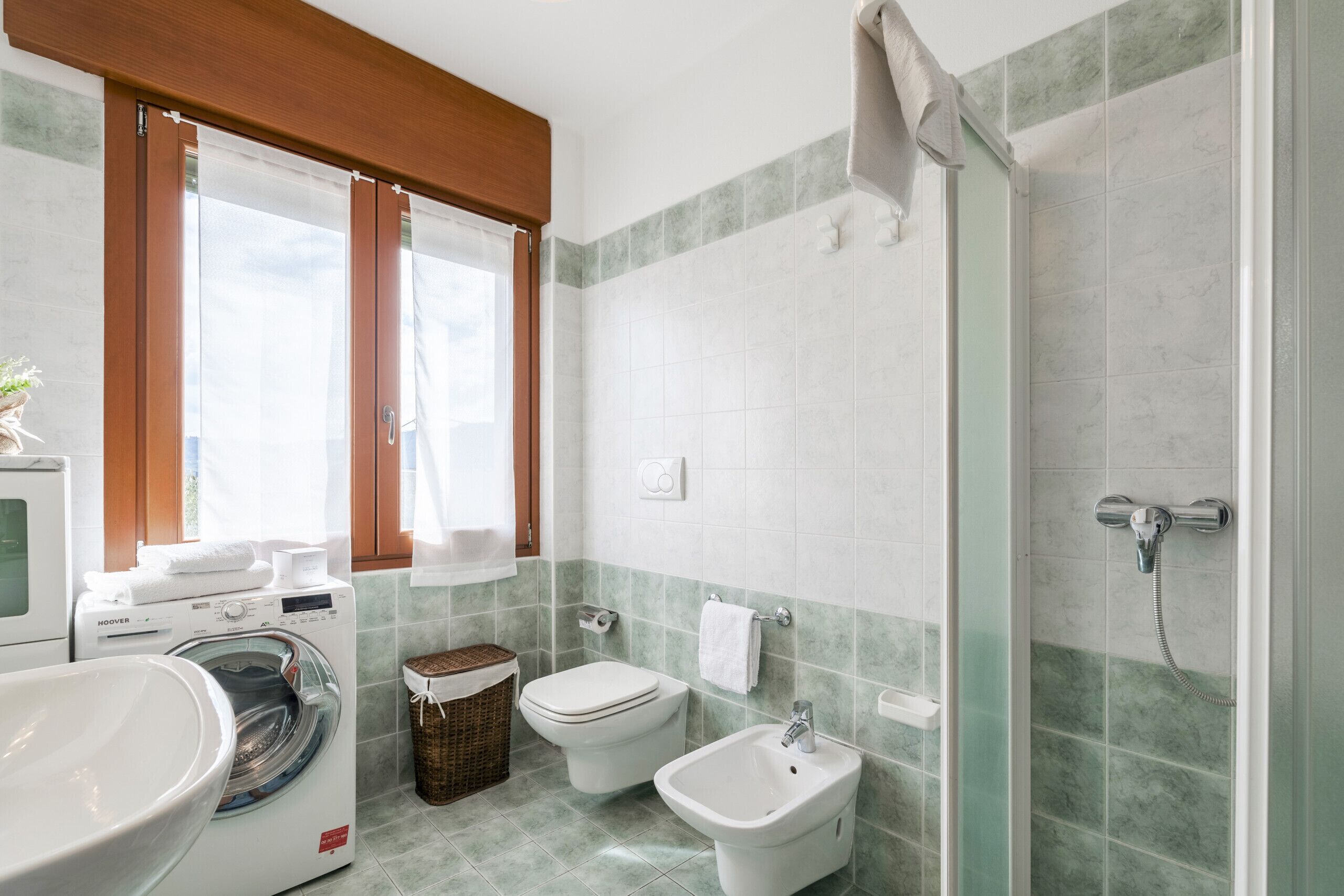 A modern bathroom with a washing machine, toilet, bidet, and a glass-enclosed shower.