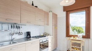 A modern kitchen with light wood cabinets, stainless steel appliances, and a view of greenery through a window. - Regarda - La Terrazza di Garda lake view apartment with terrace (Garda)