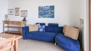 A living room with a blue sofa, a wooden table, and a painting of water lilies on the wall.