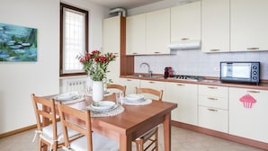 A modern kitchen with white cabinets, a wooden dining table with chairs, a vase of red flowers, and a microwave.