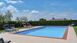 A rectangular swimming pool with a tiled deck, surrounded by lounge chairs and a bench.
