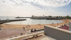 A coastal view with a sandy beach, a pier, and a building complex with a flag.
