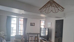 Ein Wohnzimmer mit einer Couch, einem Sessel, einem kleinen Tisch, einem Fernseher und einer Küchenzeile mit Spüle und Korb.