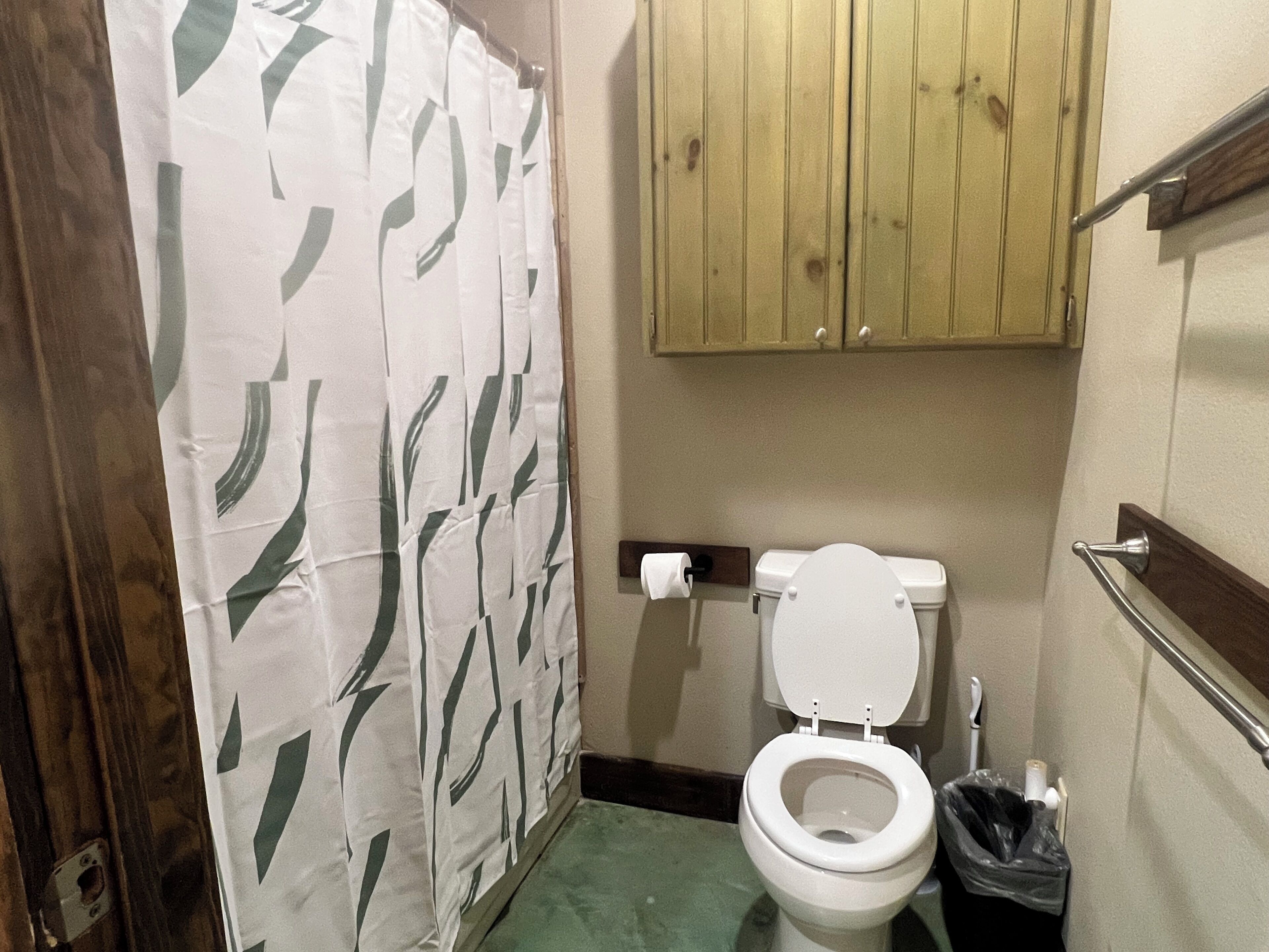 A bathroom with a toilet, a shower curtain, and wooden cabinets.