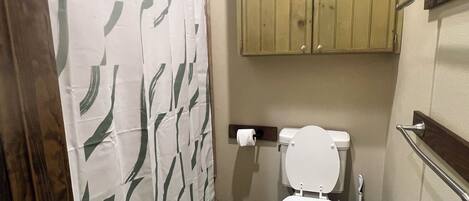 A bathroom with a toilet, a shower curtain, and wooden cabinets.