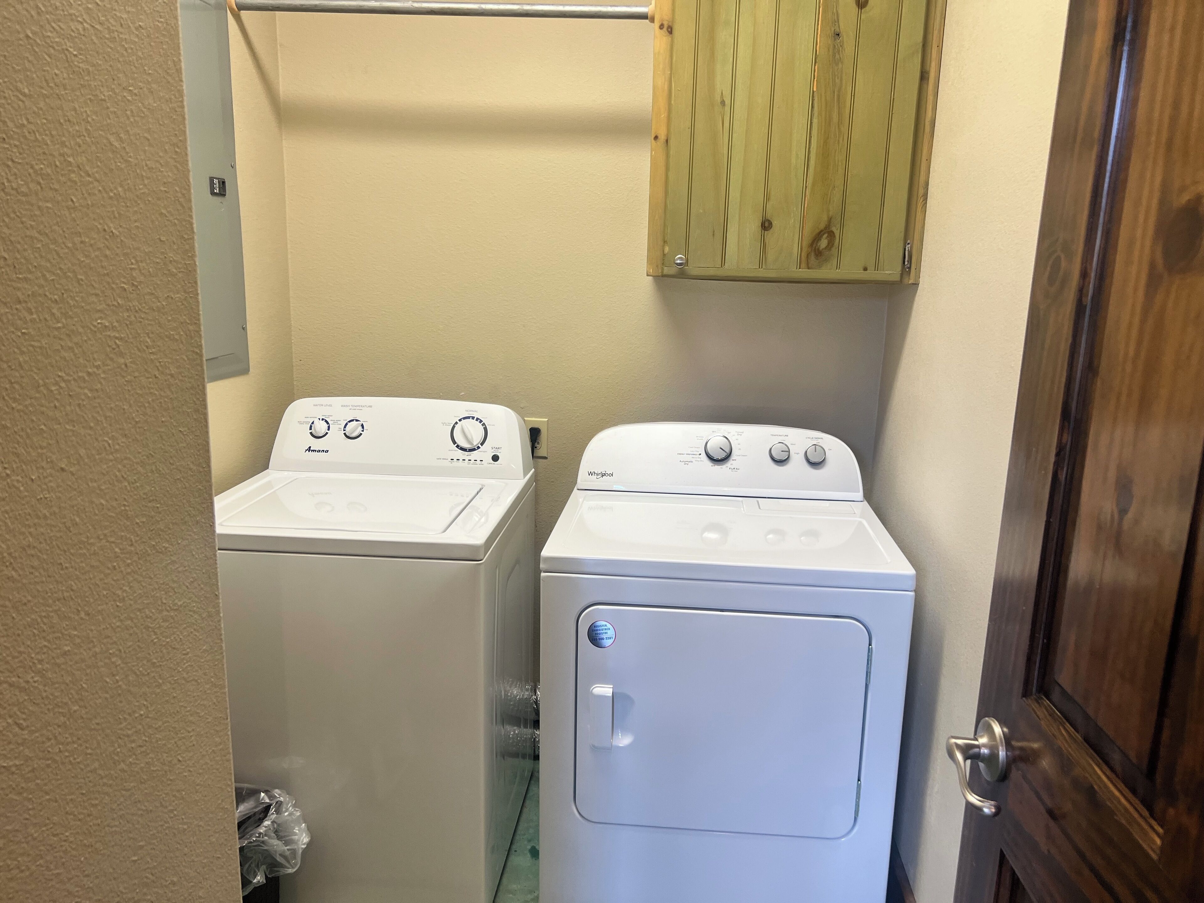 A laundry room with two white washing machines, a wooden cabinet above, and a wooden door.