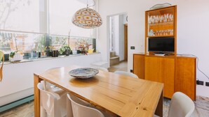 A dining area with a wooden table, white chairs, a hanging light fixture, and a cabinet with glassware. - La Rocca Sulla Cala by Wonderful Italy (Palermo)