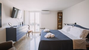 A hotel room with a bed, a dresser, a TV, a bookshelf, and a window. - La Rocca Sulla Cala by Wonderful Italy (Palermo)