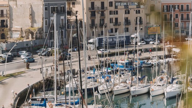 A marina with boats docked, surrounded by buildings with balconies and a dome structure in the background. - La Rocca Sulla Cala by Wonderful Italy (Palermo)