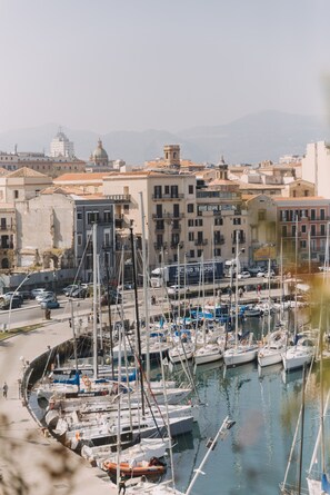 Un port de plaisance où sont amarrés des bateaux, entouré de bâtiments dotés de balcons et surmonté, au loin, d’une structure en forme de dôme.