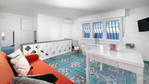 Eine moderne Küche mit Meerblick, ein Essbereich mit einem weißen Tisch und eine Wohnbereits mit einem orangefarbenen Sofa.