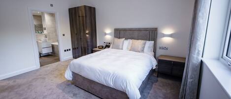 A bedroom with a large bed, a bedside table, a nightstand, a wardrobe, and a bathroom visible through an open door.