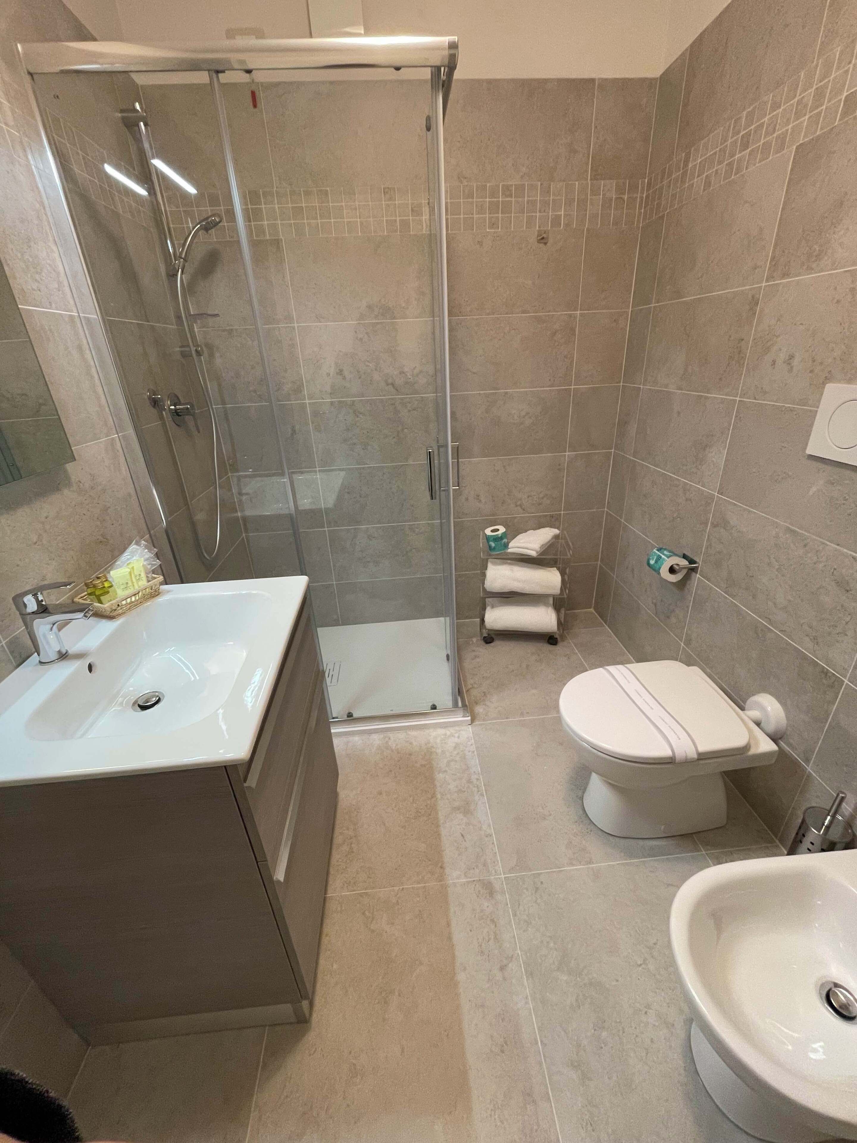 A bathroom with a glass-enclosed shower, a white sink, and a toilet.