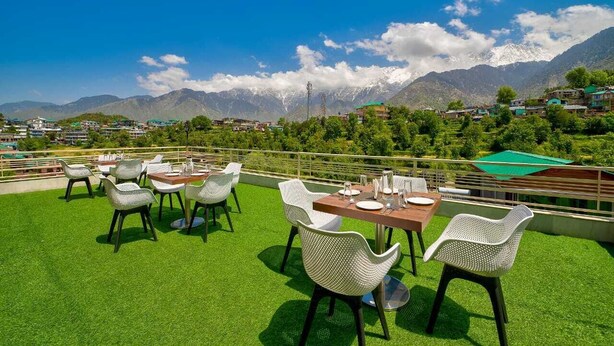 A rooftop terrace with tables and chairs, offering a view of a mountainous landscape.