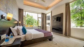 A modern hotel room with a large bed, a TV mounted on the wall, and a balcony with a view of trees.