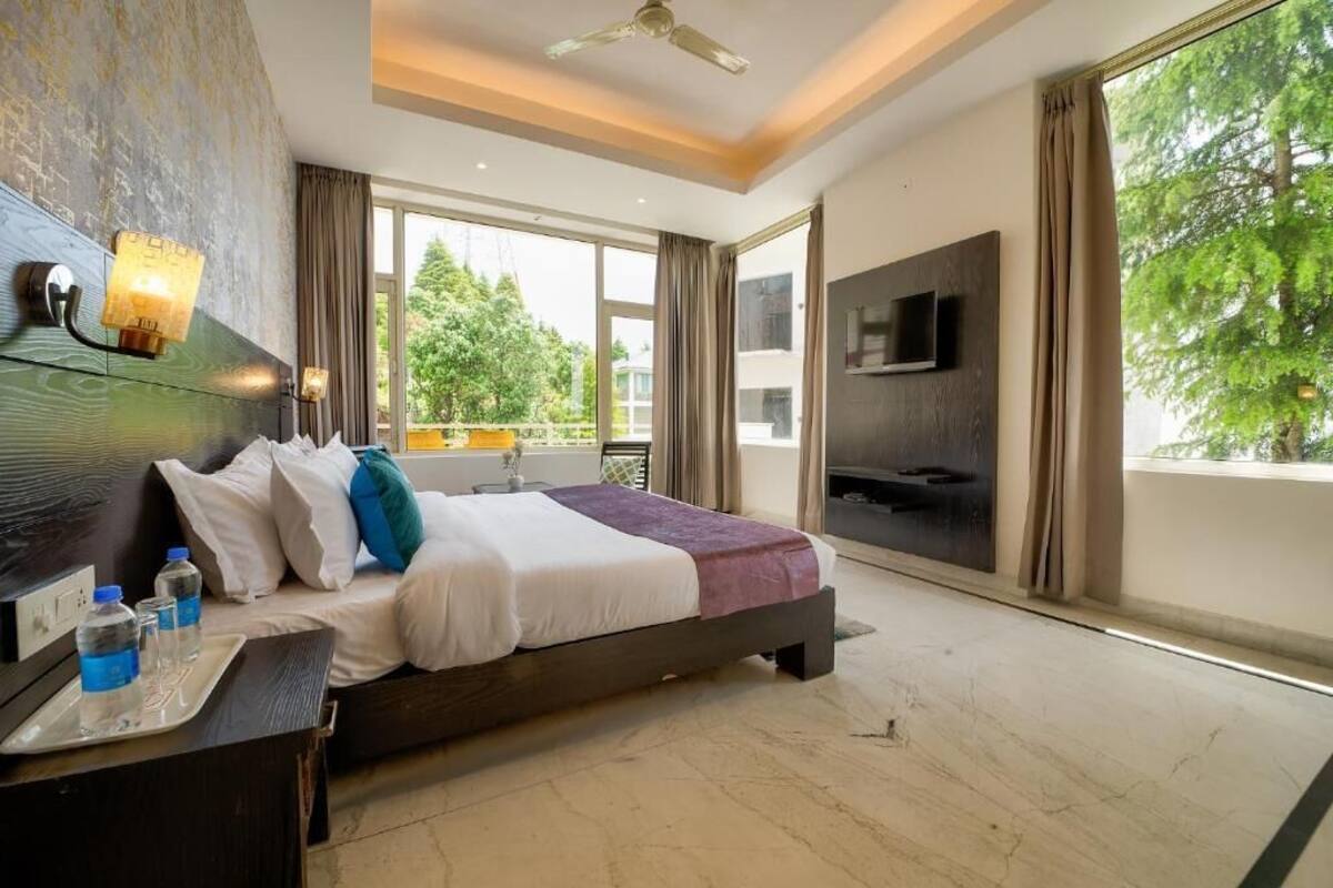 Quarto de hotel moderno com uma cama grande, TV fixada na parede e varanda com vista para árvores.