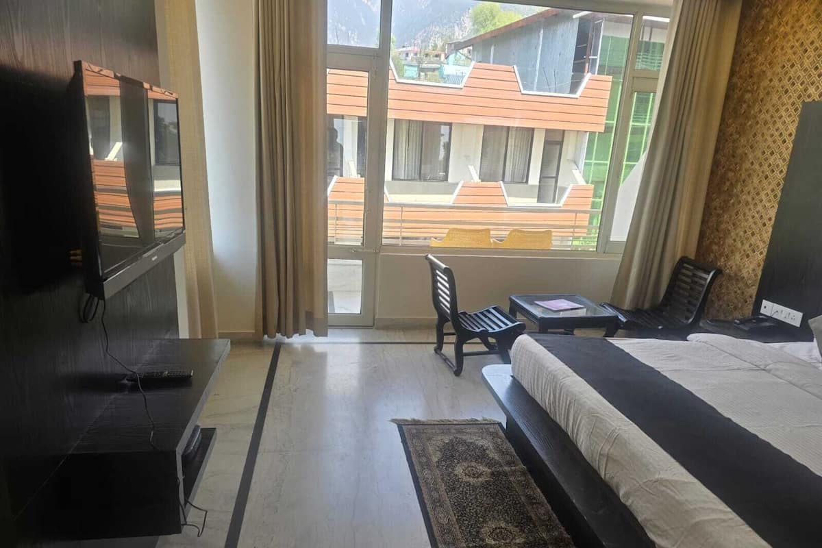 Quarto de hotel moderno com uma cama, escrivaninha, cadeira e televisão na parede.