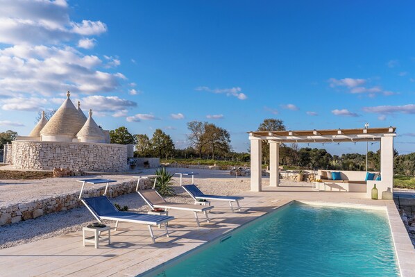 A pool area with lounge chairs, a pergola, and a stone structure with conical roofs.