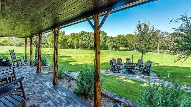 An outdoor patio with wooden beams, seating, and a view of a grassy area with trees. - Secluded Cabin in Weatherford, TX (Weatherford)