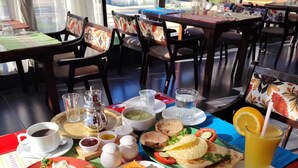 Een ontbijtbuffet met diverse gerechten, zoals eieren, toast en fruit, op een tafel met uitzicht op een zwembad en groen buiten.