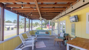 A covered porch with wooden furniture, a ceiling fan, and a TV mounted on the wall.