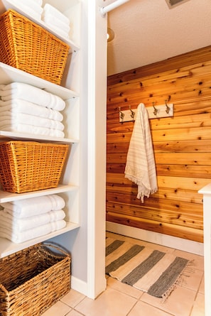Une salle de bain avec un mur en bois, un porte-serviettes avec une serviette, et des paniers en osier sur des étagères.
