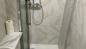 A bathroom with a glass-enclosed shower, a toilet, and a sink with a marble countertop.