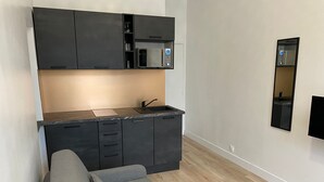 A modern kitchen with dark cabinets, a microwave, and a built-in oven. There is a grey sofa and a wooden floor.