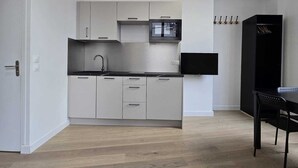 A modern kitchen with white cabinets, a microwave, and a black refrigerator. - Studio Grands Boulevards (Paris)
