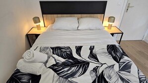 A bed with a black and white leaf-patterned duvet, two bedside lamps, and a wooden headboard. - Studio Grands Boulevards (Paris)