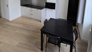 A compact kitchen with white cabinets, a black countertop, and a microwave. There's a dining table with two chairs and a hanging light fixture. - Studio Grands Boulevards (Paris)