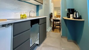 Una cocina moderna con armarios grises, un refrigerador de acero inoxidable, un horno integrado y un microondas. Hay un lavamanos con grifo, una encimera con una cesta de fruta y una cafetera en un estante.