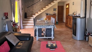 A living room with a black leather sofa, a dining table with chairs, a staircase leading to another level, and a kitchen area with a refrigerator.