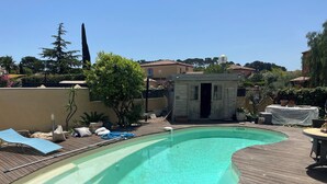 A swimming pool with a wooden deck, a small building, and surrounding greenery.