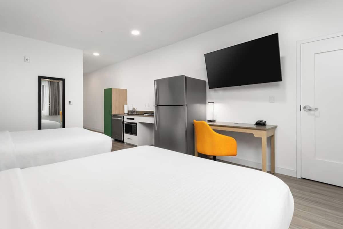 A hotel room with two beds, a desk, a TV, and a refrigerator.