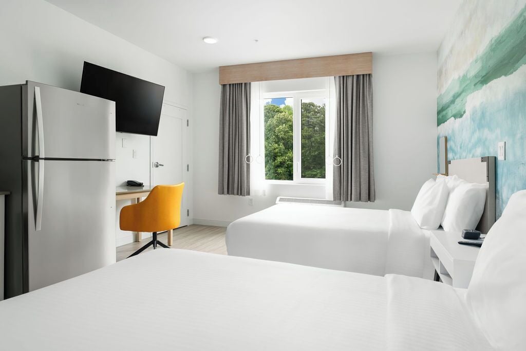 A hotel room with a bed, a desk, a chair, a TV, and a window with curtains.
