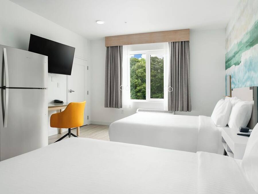 A hotel room with a bed, a desk, a chair, a TV, and a window with curtains.