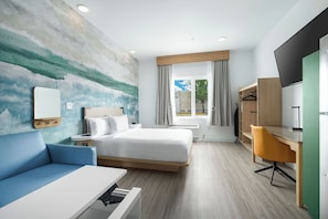 A modern hotel room with a bed, a desk, a chair, a TV, a sofa, and a large window with curtains. - YourSpace Hotels Chesapeake (Chesapeake)