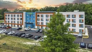 Un hotel a più piani con un parcheggio, un edificio blu con la segnaletica 'Your Space' e un edificio bianco con tocchi arancioni.